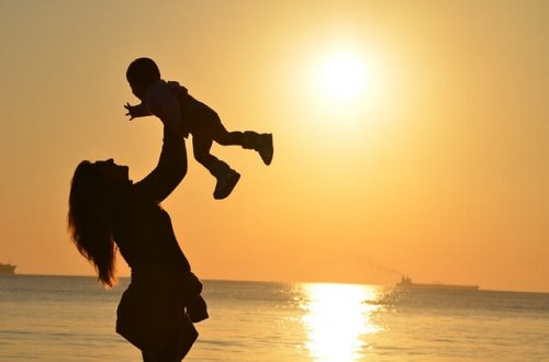 夕焼けの海で子供を抱き上げる母親